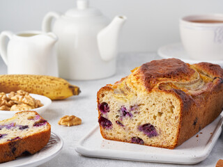 Banana bread, sliced cake with banana and blueberries. Morning breakfast with tea on light gray concrete background. Side view. 