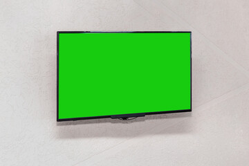 Modern TV lcd panel in black frame with blank green mockup screen hangs on white wall