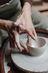 close up hand modeling pottery on a potter wheel in a cozy home workshop. Creating products from environmentally friendly clay with their own hands. Aesthetically beautiful female hands of the artist