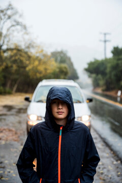 Teenage boy wearing rain jacket standing in front of minivan