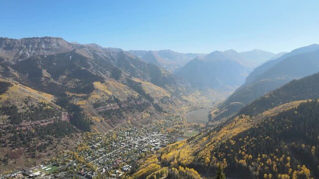 Aerial 4K video of Telluride, Colorado in autumn with beautiful fall colors. Drone clip flying forward between two trees to reveal the picturesque valley and town below.
