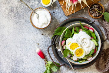 Fresh spring food, healthy vegan lunch bowl. Spinach, cucumber, radish salad and boiled eggs with sour cream. Top view flat lay. Copy space.