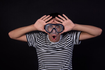 Funny young man in a sailor suit. Diving mask and snorkel. Striped clothing. Black background.