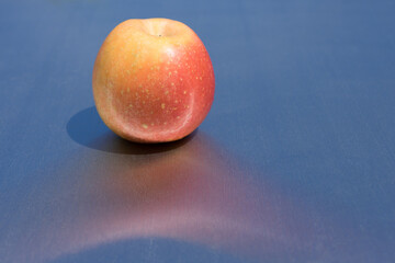 fresh tasty apple in the sun and reflection on clean blue metallic background