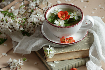 Spring floral herbal mint tea with flower buds of apple tree and quince flowers , vintage retro composition and still life with books and blooming branches, closeup, copy space, easter concept
