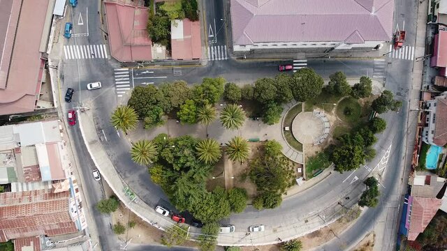 Aerial view from drone of Plaza Bismark and Avenida Alemania street at Cerro La Loma, Valparaiso, Chile. Cars driving down street around city park with palm trees. View directly above.