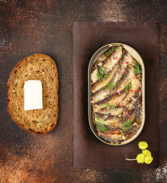 Open tin of Baltic sprats in oil with spices, a slace of bread with butter on an old brown background. Fish appetizer with beer. Traditional baltic, scandinavian food, flat lay