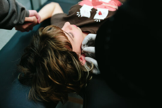 Closeup of a piercer putting the needle through a teen girl's earlobe