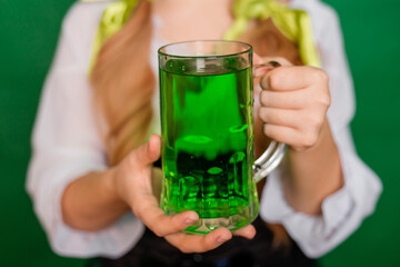 Close up, selective focus of a mug with green beer in the hands of a waitress isolated on a green background.