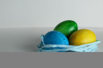 Three colored blue yellow green eggs lie in the nest on a white background with a place to text a copyspace view from the side of Von Easter