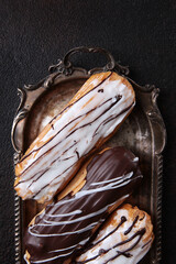 Two types of eclair on an antique tray. Dark background. Vertical photo. Classic dessert.