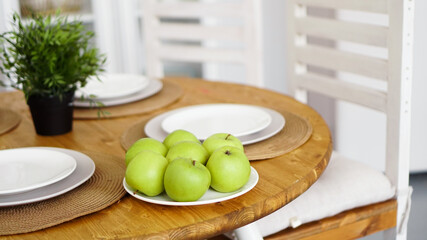 Green apples on a white plate on a wooden table. White modern scandinavian interior