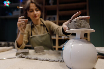 A beautiful young Caucasian woman weighs a piece of gray clay on the scales. A woman checks the weight of a piece of clay to make mugs and plates. Creative master class. Handmade