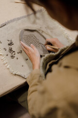 A Caucasian woman cuts out on a clay plate in a pottery workshop. Handmade pottery from clay. Creative masterclass