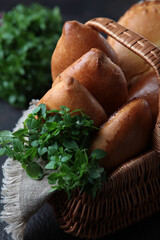 In a wicker basket are baked goods . Green basil. Photo on a dark background. Vertical photo.