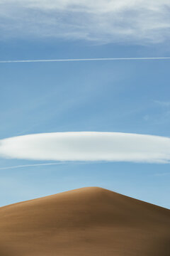 wispy clouds and chem trails frame a single golden sand dune