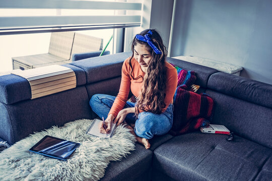 Young casual woman is sitting on couch and writting in notebook