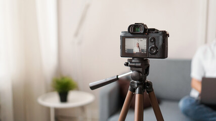 Woman blogger recording video indoors, selective focus on camera display. Space for text