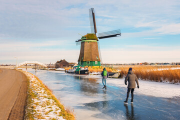 Two Ice Skaters skating on a frozen polder ditch in Opmeer, Netherlands on a cold February day in...