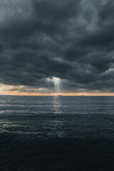 Una nave merci nel mare illuminata da un raggio di sole tra le nuvole di pioggia