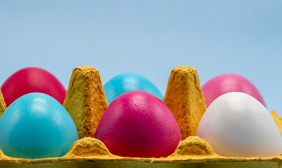Easter background. Close-up of colorful Easter eggs in a bright cardboard egg box on a blue background. Free space. Easter composition, bright color, healthy product, festive mood.
