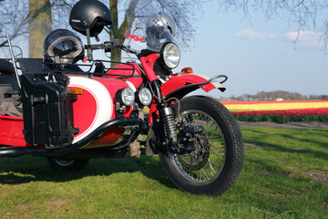 Close up of a parked red motorcycle with sidecar and tulip fields