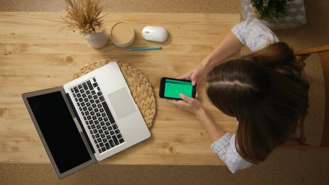 The girl is surfing on the Internet. Social network. The green screen of the phone monitor. A laptop. Top view. Remote training.