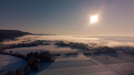 Aerial view over amazing winter wonderland bavarian landscape with fog and sunlight on beautiful winter day