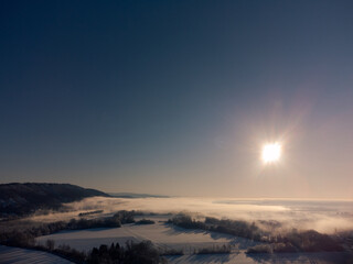 Aerial view over amazing winter wonderland bavarian landscape with fog and sunlight on beautiful winter day