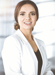Portrait of young successful businesswoman, while she is standing near the desk in a sunny modern office. Business concept