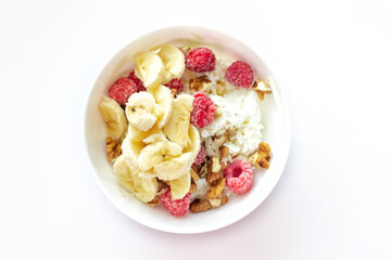 Close-up of a healthy breakfast with fruit in a white bowl. Cottage cheese with banana, raspberries, yogurt and walnuts. Top view