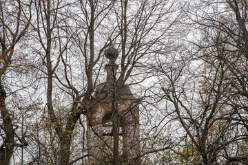 An abandoned, dilapidated Orthodox church in the fall among the bare branches of trees.