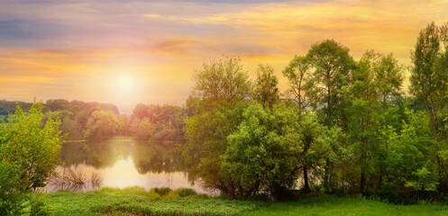 Summer landscape with trees by the river and picturesque sky during sunset, panorama