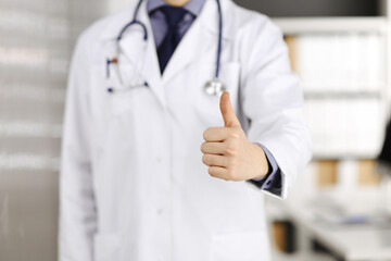 Unknown male doctor standing with thumbs up sign in clinic near his working place, closeup. Perfect medical service in hospital. Medicine and healthcare concept