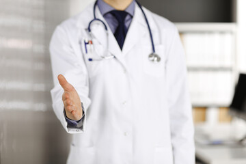 Unknown male doctor standing straight and offering helping hand in clinic near his working place, closeup. Perfect medical service in hospital. Medicine and healthcare concept