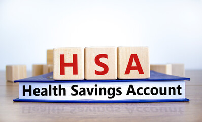 HSA, health savings account symbol. Wooden cubes on book with words 'HSA, health savings account'. White background. Medical and HSA, health savings account concept. Copy space.