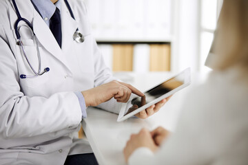 Unknown male doctor and patient woman discussing current health examination while sitting in clinic...