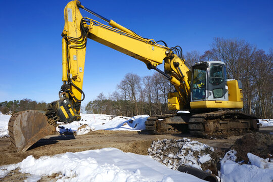 Bagger, Raupenbagger, Kettenbager auf einer sandigen Baustelle im Winter mit Schnee