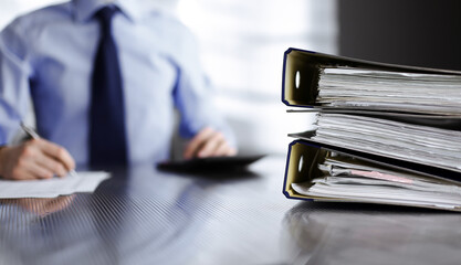 Binders with papers are waiting to be processed by man accountant in blue shirt staying at home...
