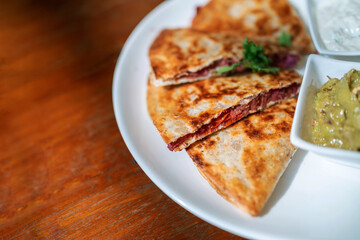 Close-up of Vegan Quesadilla: grilled whole-wheat tortilla filled with sweet potato and red bean, vegan quesso cheese served with guacamole salsa and Tzaziki sauce.