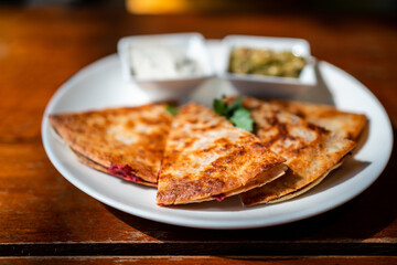 Close-up of Vegan Quesadilla: grilled whole-wheat tortilla filled with sweet potato and red bean, vegan quesso cheese served with guacamole salsa and Tzaziki sauce.