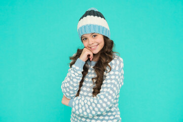 cheerful kid girl with long curly hair in knitted hat and sweater on blue background, beauty