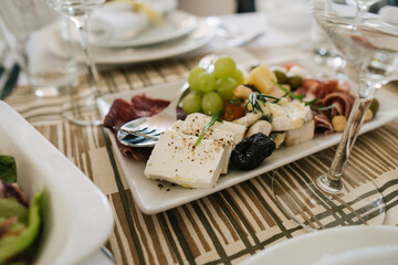 Side view of a decorative appetizer in white bowls of cheese, grapes and meat as part of the restaurant menu. Close-up of cheese