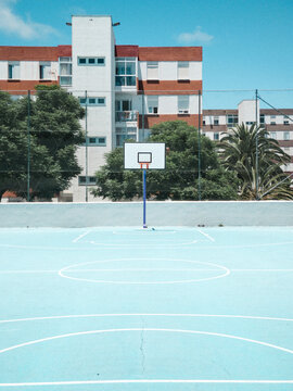 Basketball goal on blue court against blue sky and colorful buildings