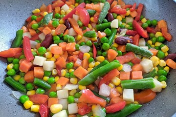 Vegetables frozen in pan for stew. Fresh vegetables food background - green beans, corn, red pepper, pea. Mixed frozen vegetables. Frozen cut veggie mix deep cool. Healthy vegetarian concept top view