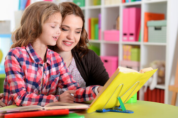 Fototapeta premium Portrait of a beautiful little cute girl with mother doing homework