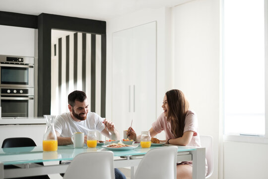Happy young couple having breakfast at dining table in rental house