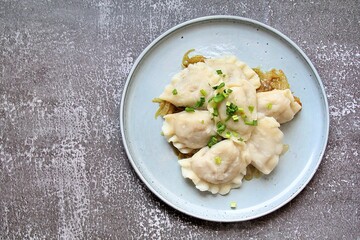 round plate, hot steaming dumplings on a fried onion pillow, carbohydrates on a plate, dumpling dough, hot dumplings sprinkled with green onions, steam over warm food
