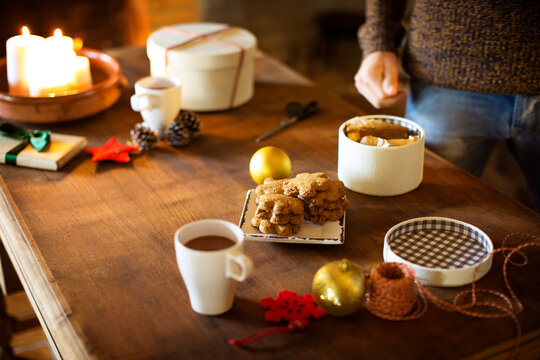 Cropped image of man preparing gift box while having cookies and coffee at table