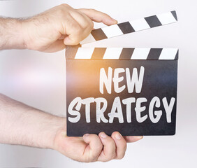 Obraz premium On a white background, a man holds a clapperboard in his hands on which it is written - NEW STRATEGY